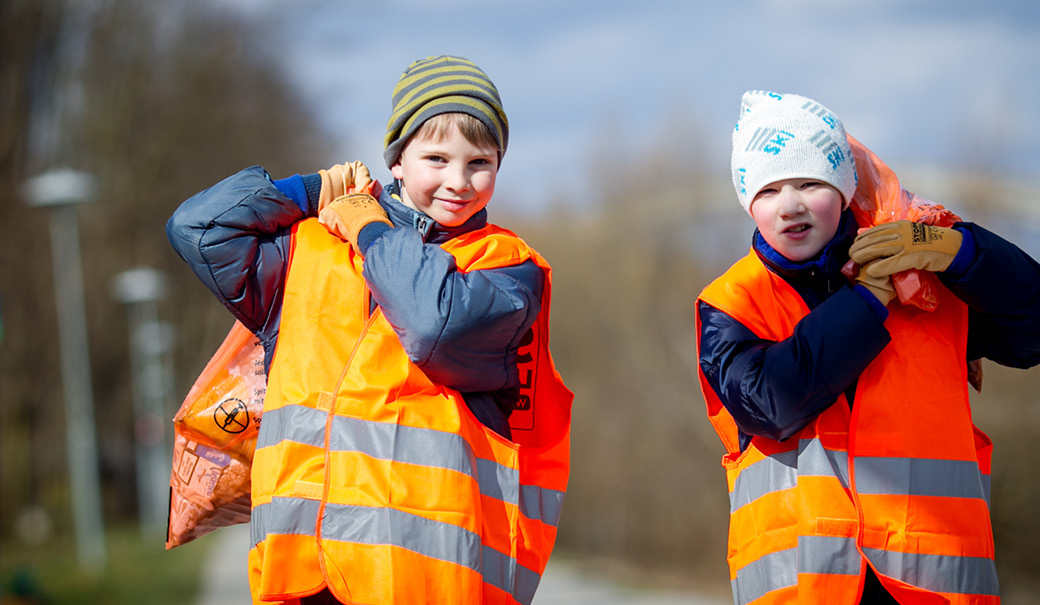 zwei Kinder in Warnwesten tragen Müllsäcke der Frühjahrsputz-Aktion